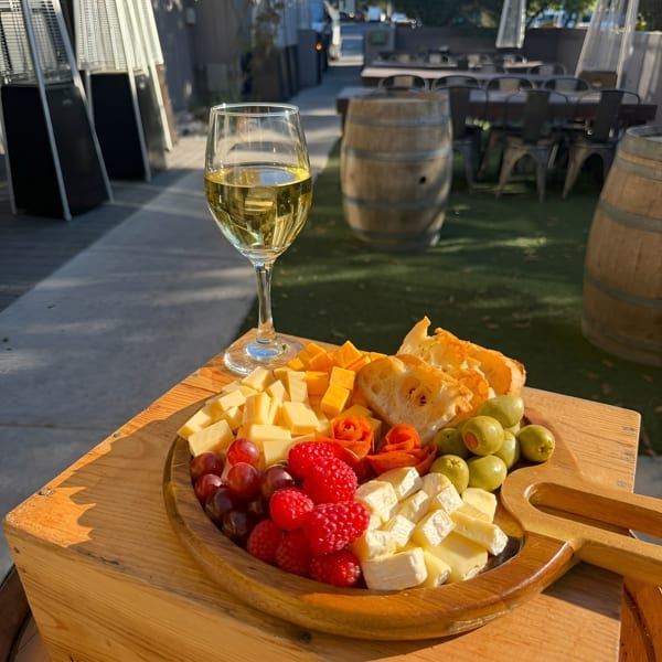 Charcuterie board with cheese, fruit, olives, and bread next to white wine on an outdoor patio.