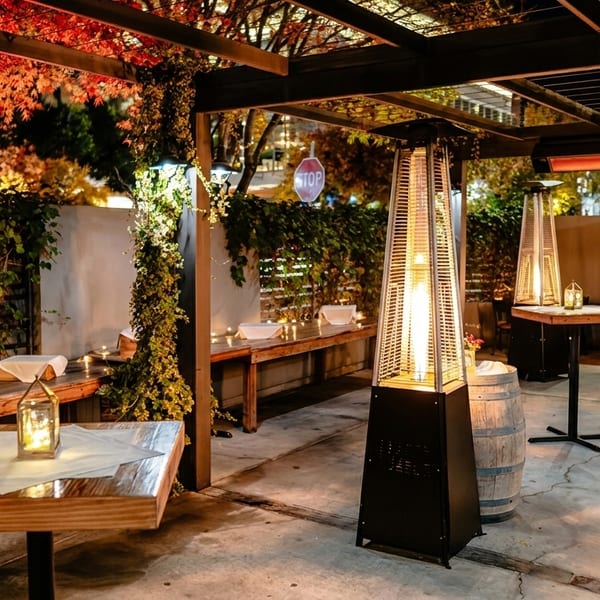 An inviting outdoor patio at night, with warm lighting, heaters, and lush greenery.