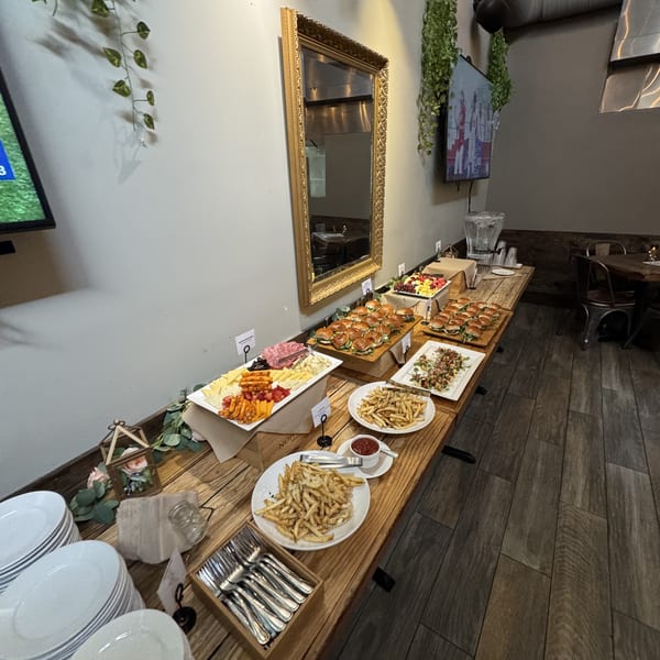 Restaurant buffet with sliders, charcuterie, french fries, and fruit on a rustic wooden table.