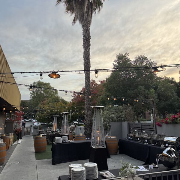 Outdoor restaurant patio set for an event with buffet tables, patio heaters, and string lights.