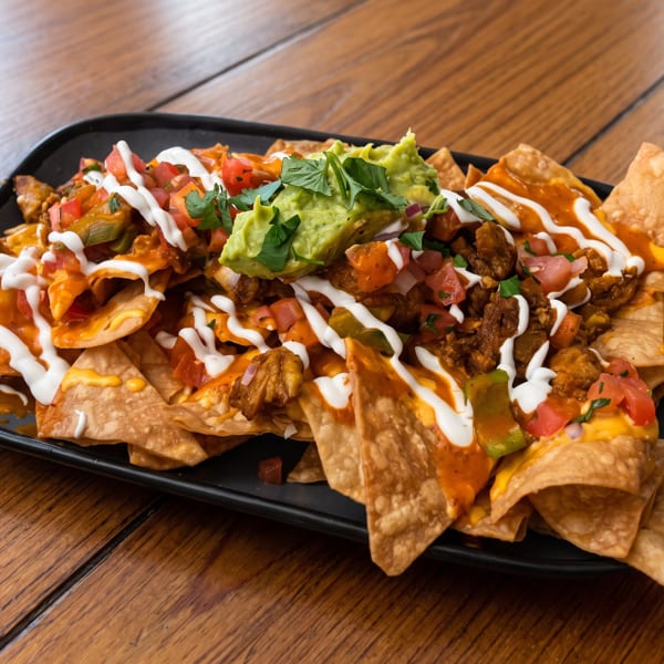 Loaded nachos with cheese, meat, salsa, sour cream, guacamole, and cilantro on a black plate.