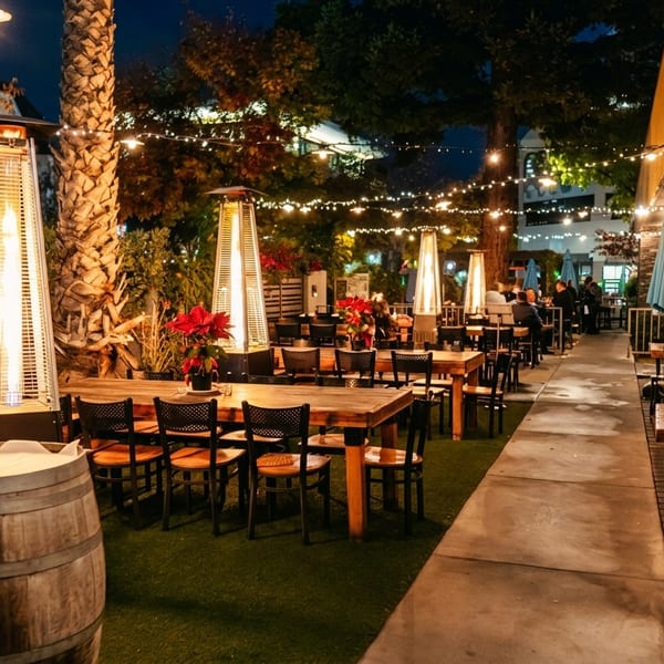 Outdoor restaurant patio at night with string lights, patio heaters, and dining tables.