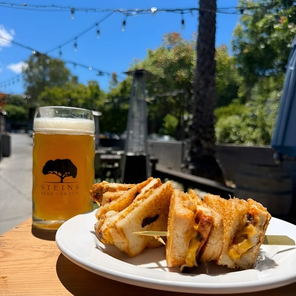 A Steins Beer Garden beer and grilled cheese sandwiches on an outdoor patio table.