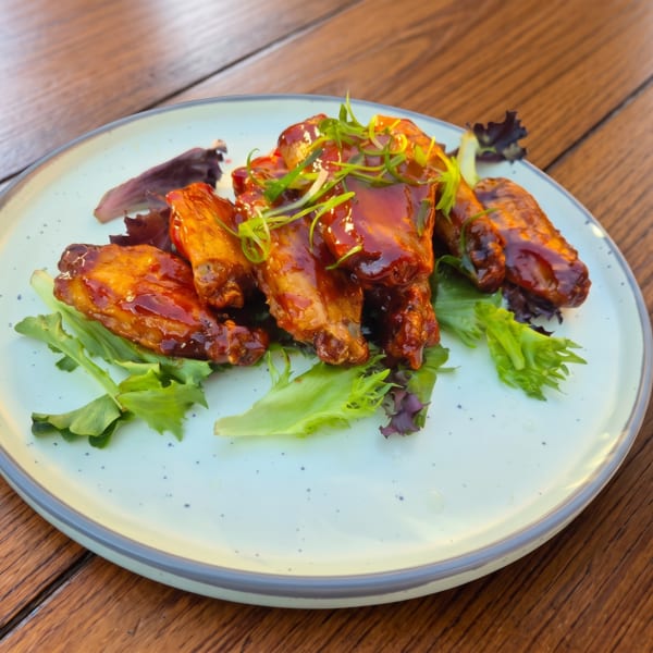 Glazed chicken wings with green onions and lettuce on a light plate set on a wooden table.